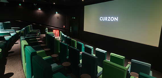 Screening room with green seats facing an illuminated Curzon screen