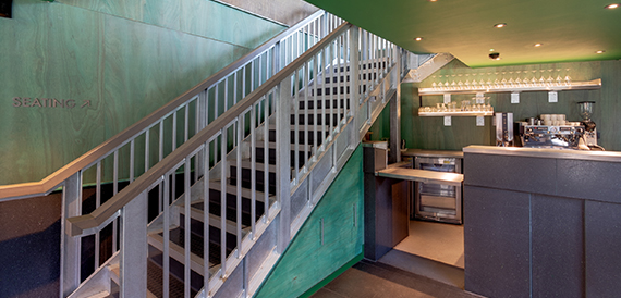 Green-panelled staircase with a decorative grille railing and wine rack