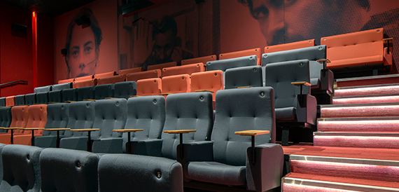 Cinema auditorium with grey seats beside red-lit steps and a portrait mural