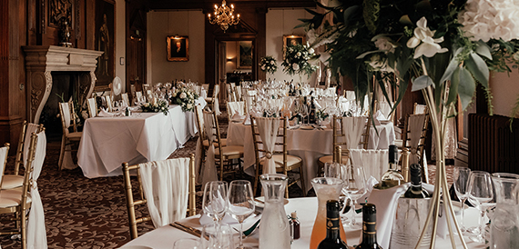 Dining room set with white tablecloths, wine glasses and flowers beside the fireplace