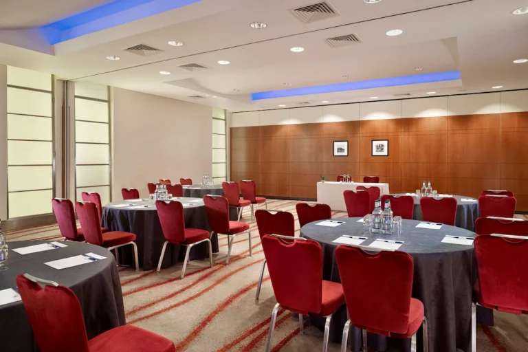Albert 2 meeting room with round tables, red velvet chairs and a wood-panelled wall with framed photos.