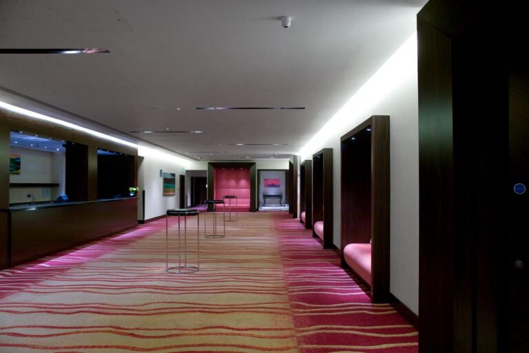 Ballroom pre-function area with striped patterned carpet, pink lighting and high tables.