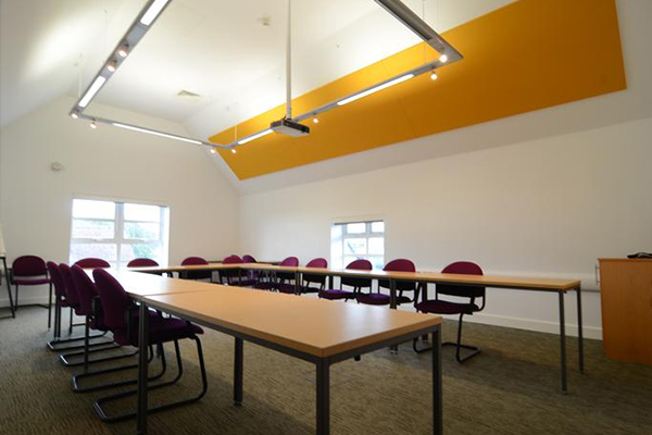 Small boardroom with a long table, maroon chairs and a yellow ceiling accent