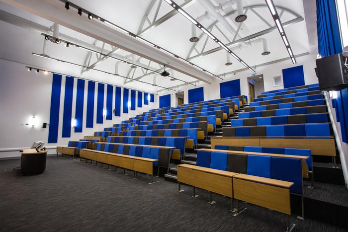 Tiered lecture theatre with blue seating and blue acoustic wall panels
