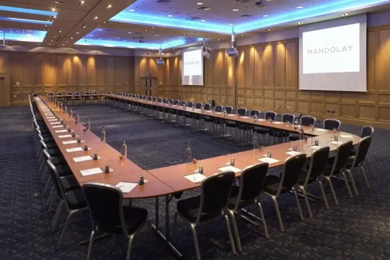 Mandolay Suite set with a long U-shaped conference table facing a projector screen