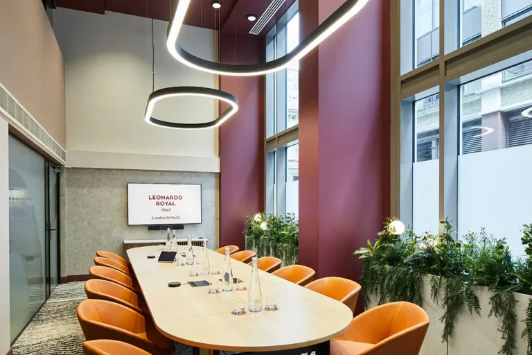 Meeting room with an oval table, orange chairs and a wall-mounted screen
