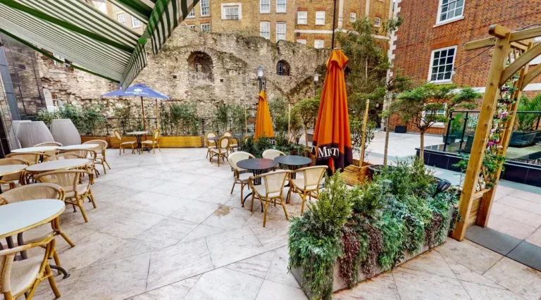 Outdoor Piazza terrace with orange parasols and seating by a brick ruin wall