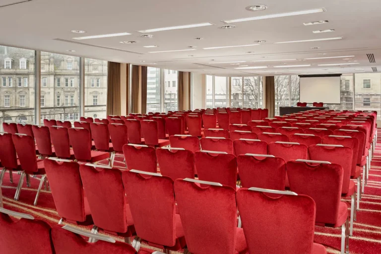 Large theatre-style auditorium with rows of red velvet chairs facing a projector screen.