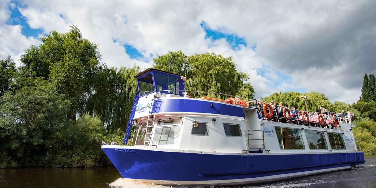 River Prince boat with passengers on the upper deck cruising past trees