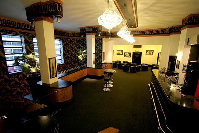 Art deco lounge bar with chandeliers, a curved counter and black stools