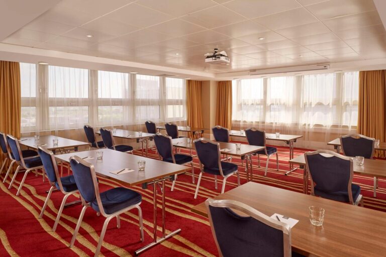 Meeting room laid out theatre-style with rows of desks, navy chairs and gold curtains.