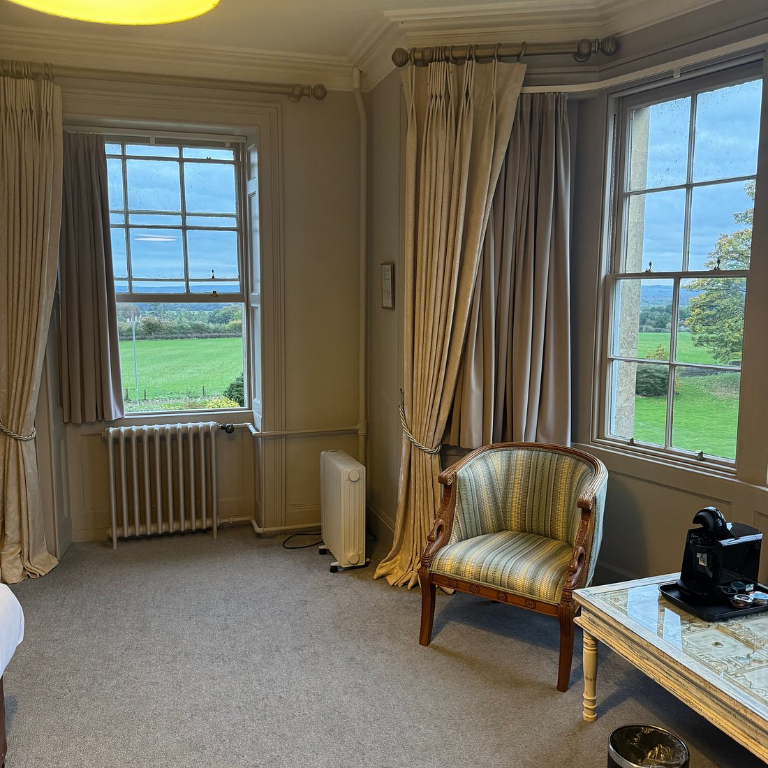 Hotel bedroom with a striped armchair and countryside views through the windows