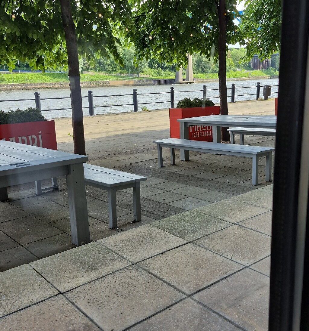 Outdoor terrace tables and benches beside the riverside promenade